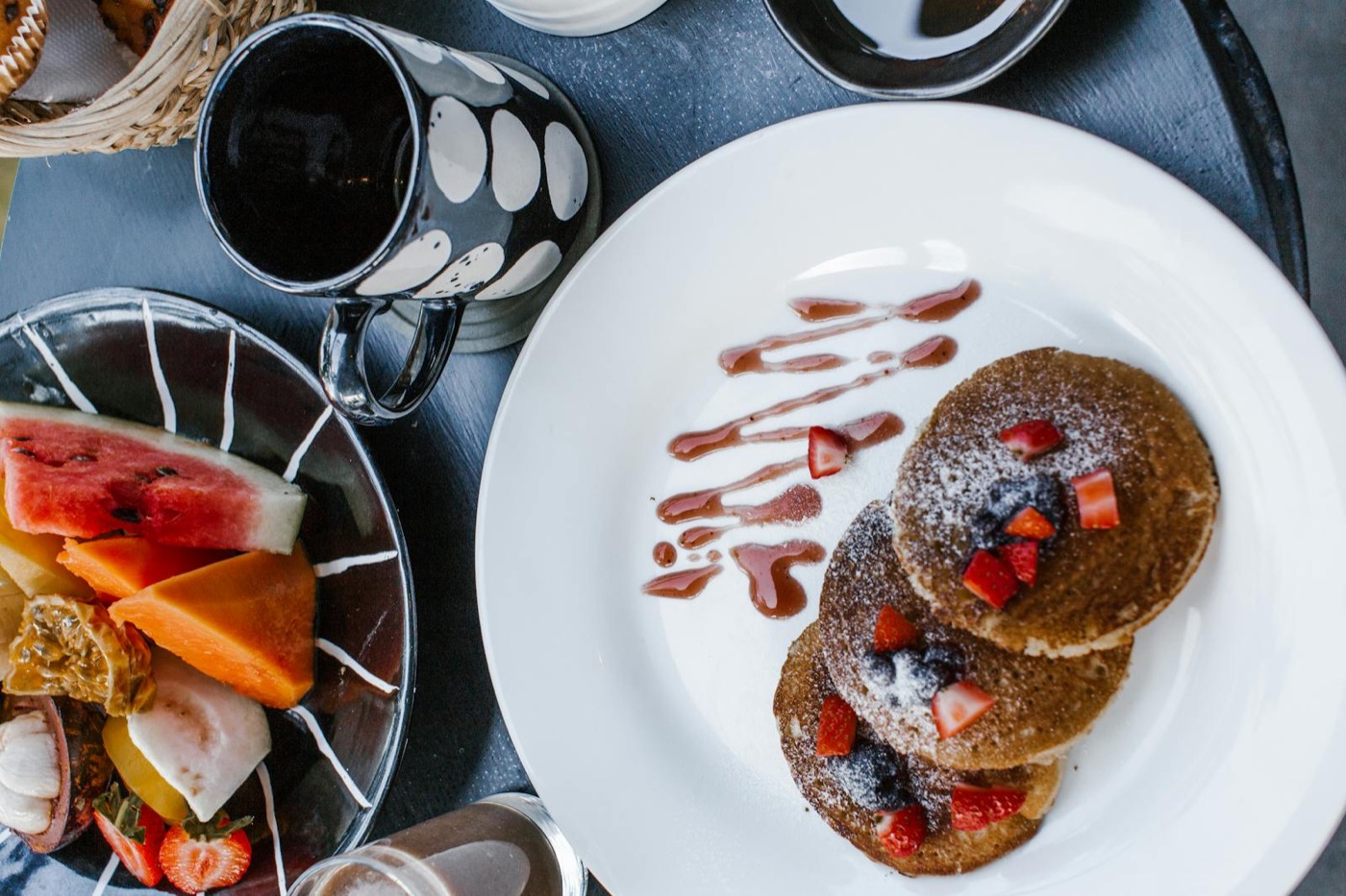 Mise en scène chef privé : pancakes saupoudrés, fruits frais et tasse en céramique pour dîner intimiste