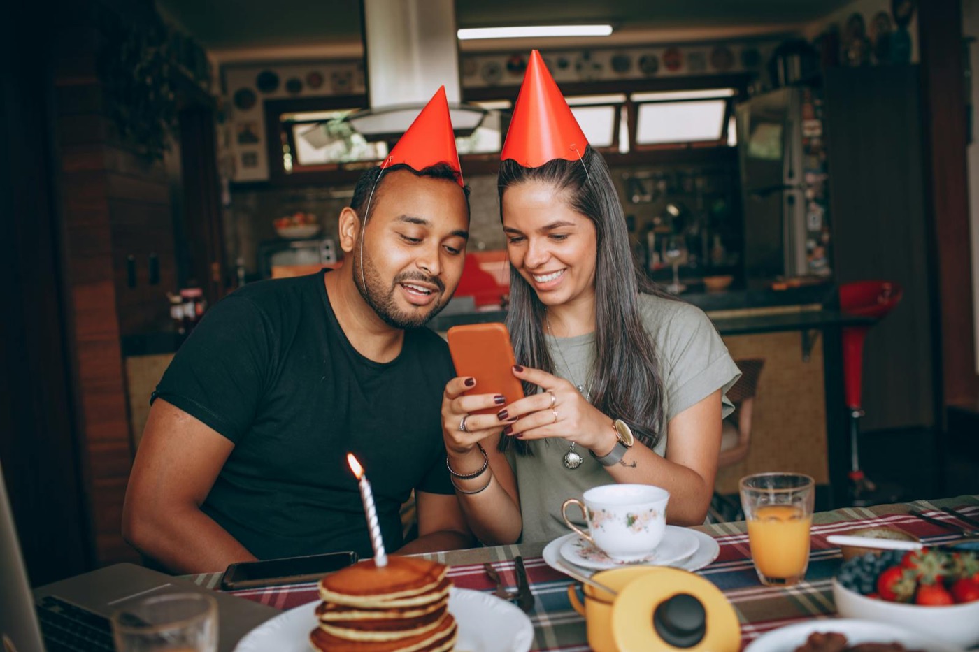 Couple à table avec chapeaux de fête, bougie sur pancake, célébration intime brunch d'anniversaire