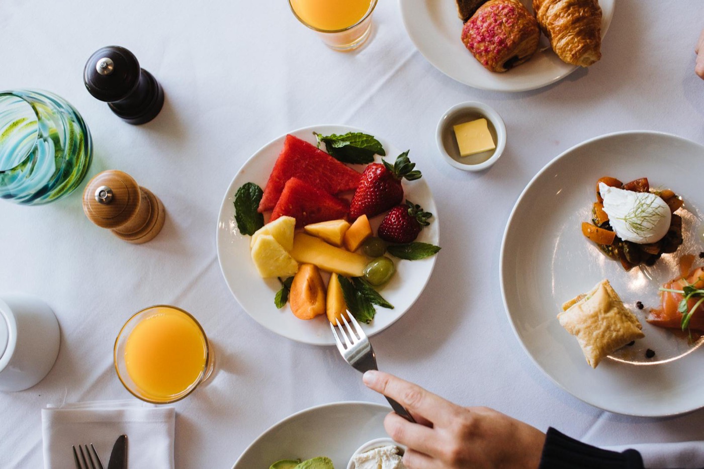 Vue overhead d'une tablée brunch avec viennoiseries, fruits frais et jus d'orange entre amis