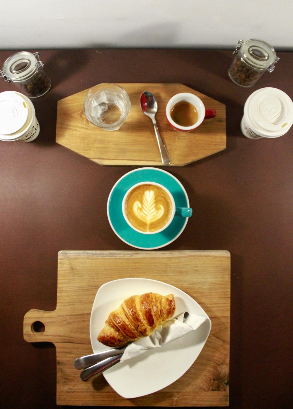 Café cortado avec latte art, cappuccino et croissant sur planche bois — flat-lay boutique de quartier