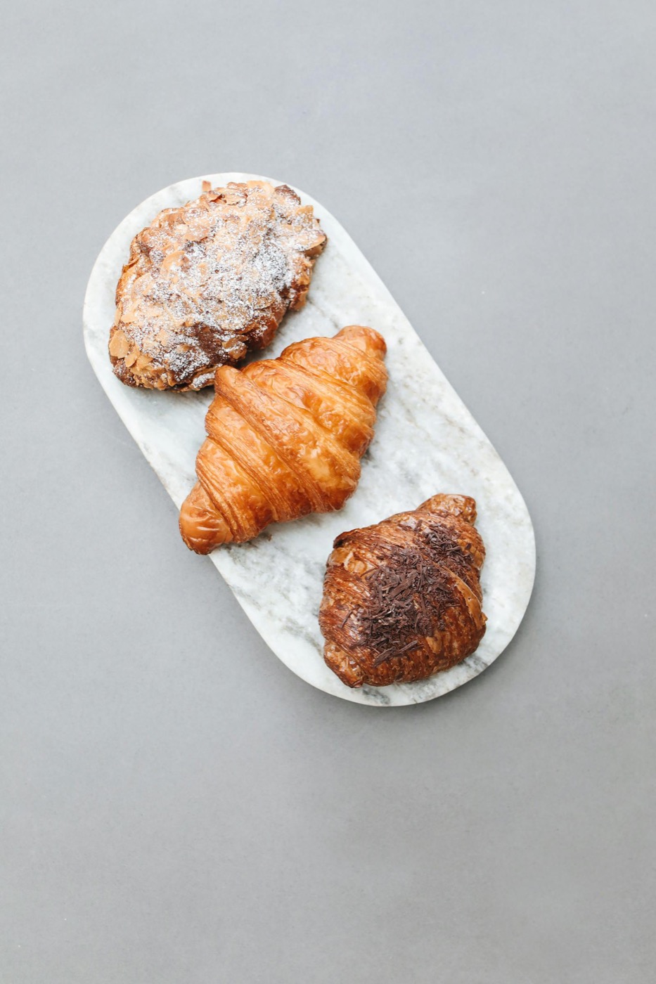 Trois viennoiseries — croissant amande, nature et chocolat — sur plateau marbre