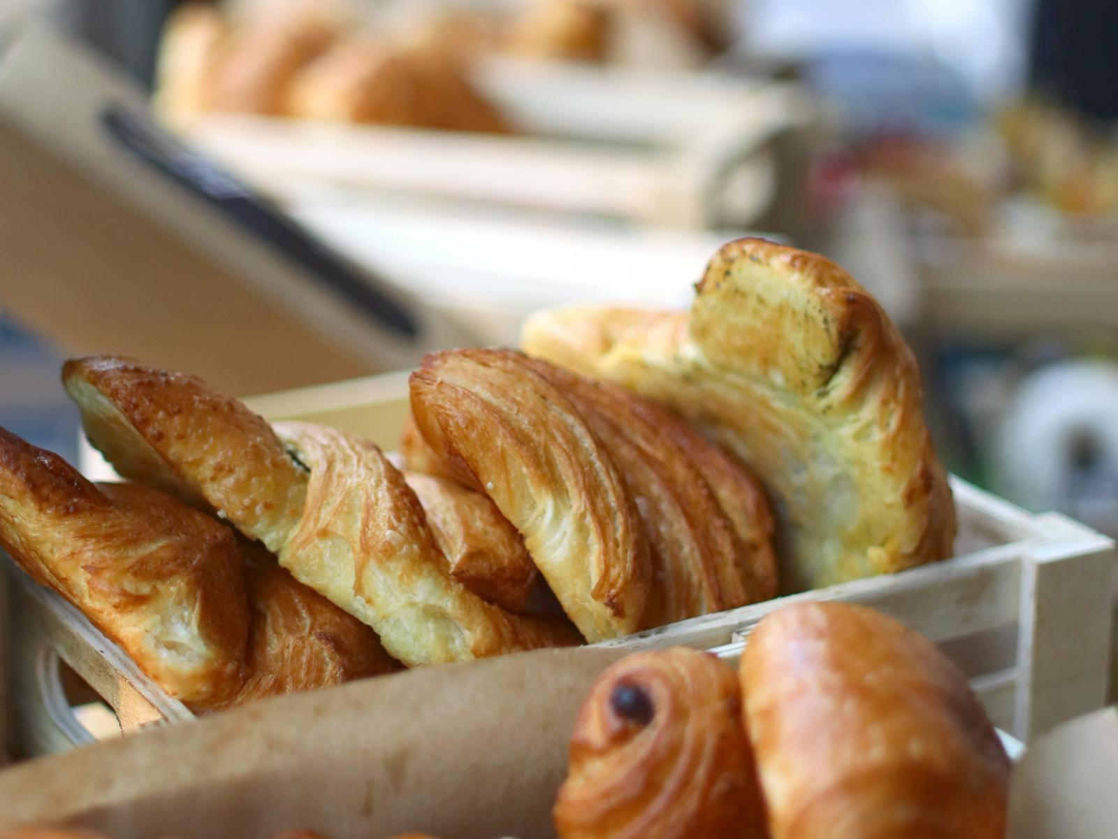 Caisses en bois remplies de croissants dorés et pains au chocolat artisanaux — viennoiseries livrées en barquettes naturelles